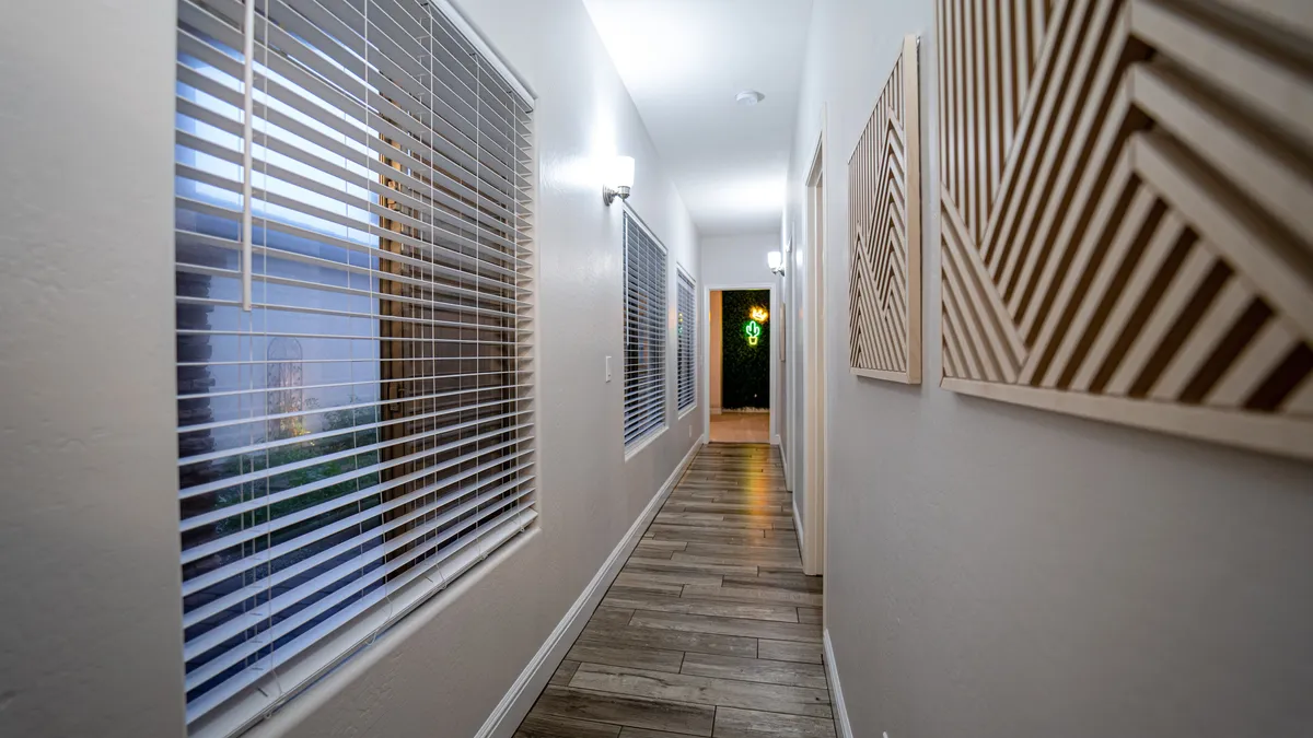 A welcoming hallway with sliding windows, decorative wall panels, and warm light fixtures. The scene captures the anticipation and hospitality of entering a cozy and well-designed living space, hinting at the comfort and care guests can expect.