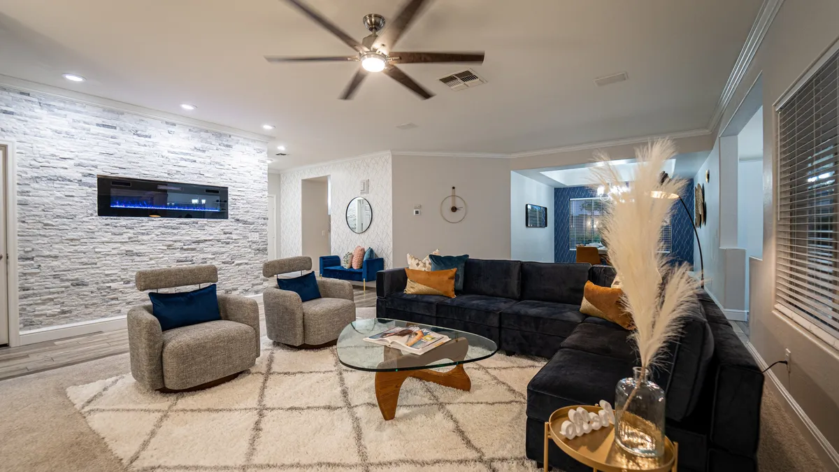 An elegant main gathering area featuring a modern electric fireplace set in a stone feature wall, a generous sectional sofa, and a glass coffee table. The space is both cozy and stylish, designed for intimate conversations or entertaining guests.