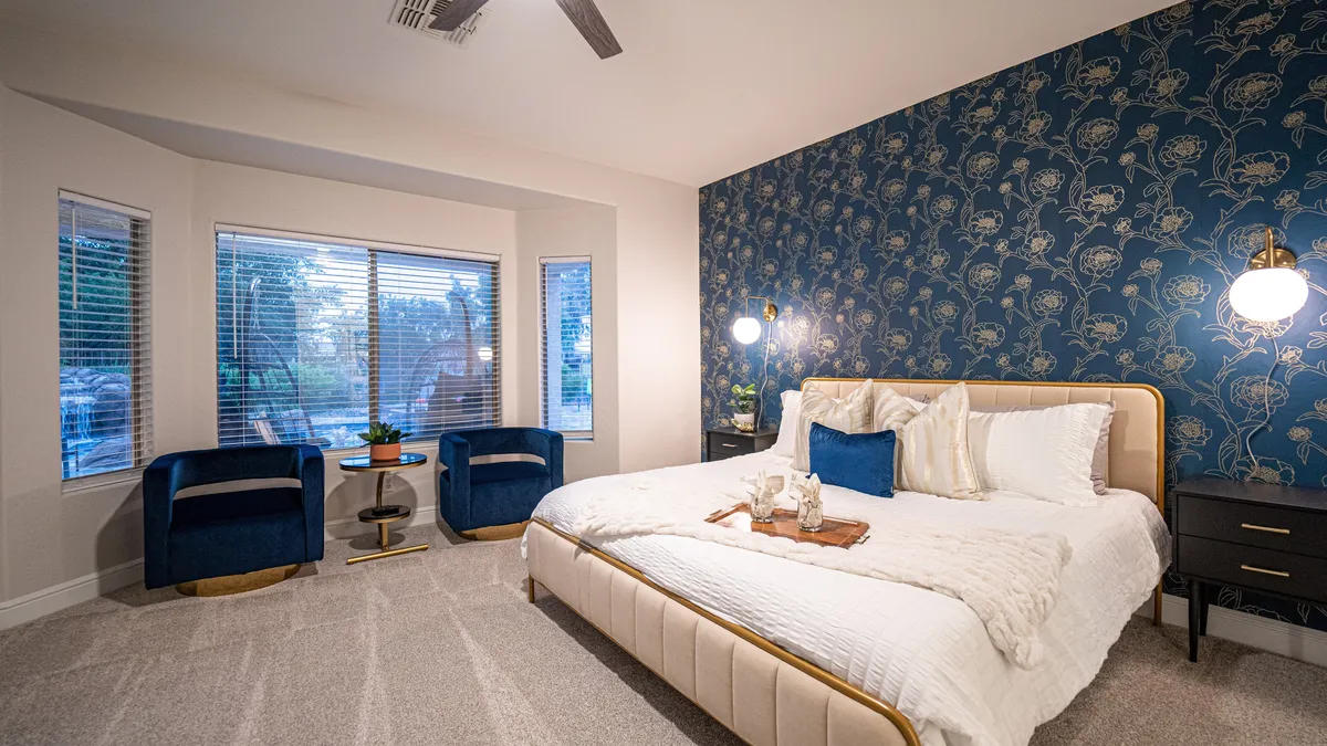 A serene bedroom with a plush bed dressed in premium bedding, a decorative accent wall adding personality, and a cozy seating area with chairs. Natural light streams in, creating a comforting and peaceful atmosphere.