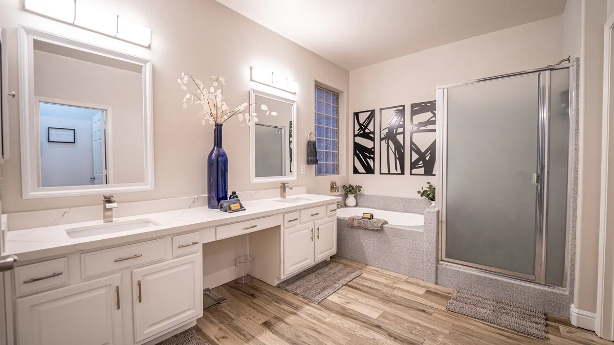 A tranquil bathroom scene with a double sink vanity, a large relaxing bathtub, a shower enclosure, and tasteful artwork. The space is inviting for both unwinding after a busy day and refreshing morning routines.