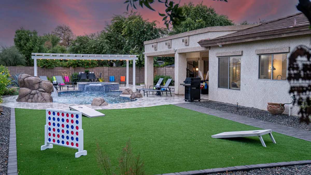 An inviting backyard scene with a swimming pool, outdoor seating, lawn games, and landscaped rocks. The setting is playful and energetic, suggesting both casual recreation and organized fun, with sunset views that invite gatherings into the evening.