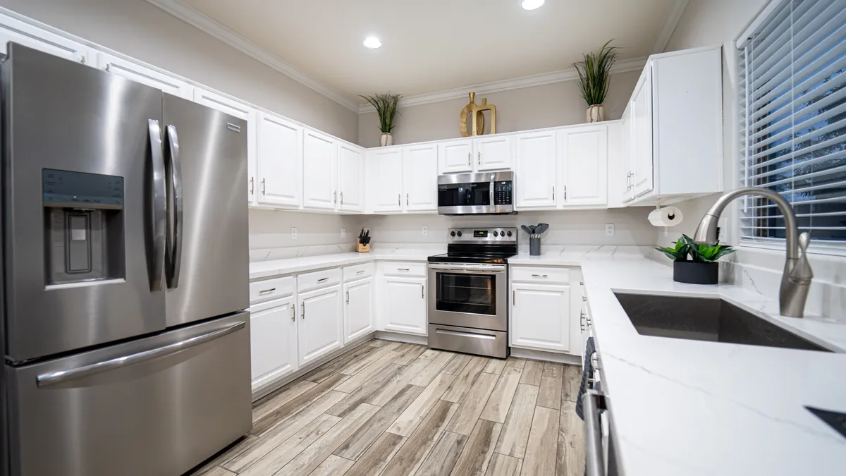 A contemporary kitchen featuring a stainless steel refrigerator, black stove, white cabinetry, and elegant marble countertops. The space is open and inviting, with plenty of room for meal prep and socializing, making it ideal for collaborative cooking and entertaining.