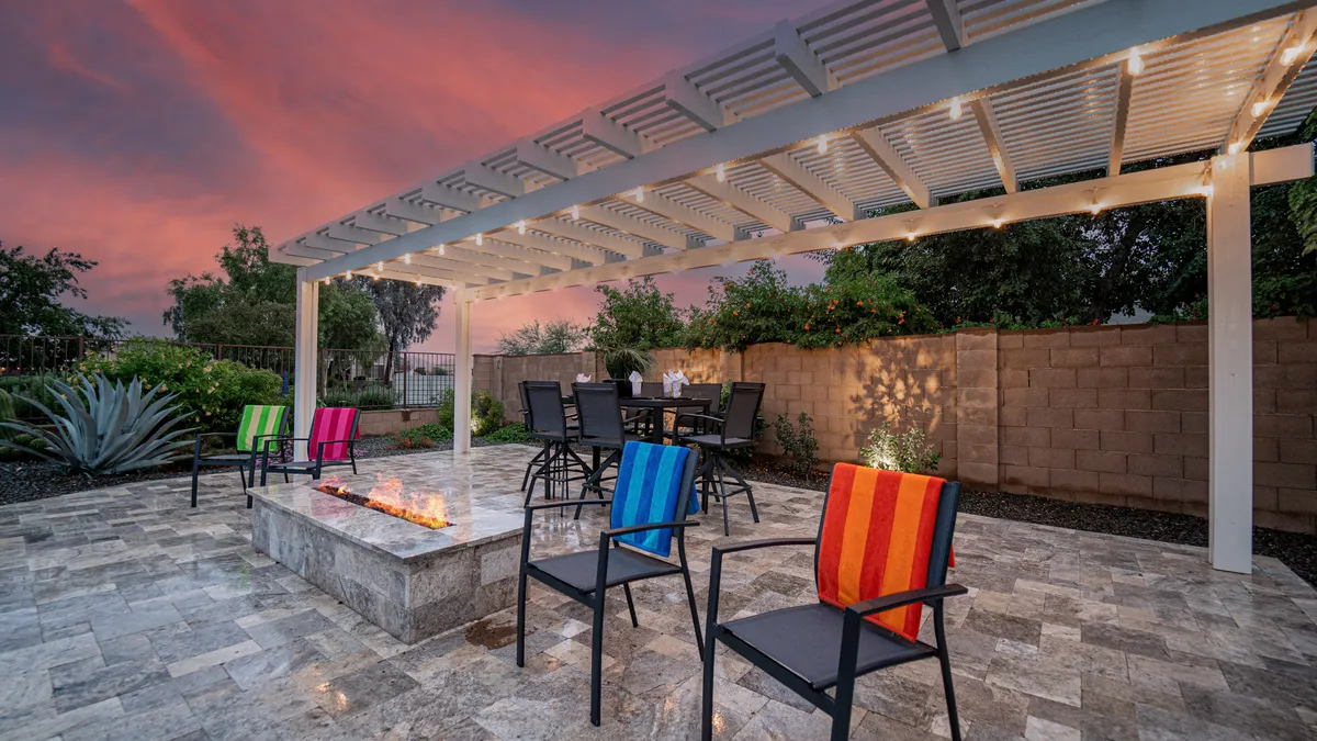 A cozy and stylish outdoor gathering area with a fire pit, pergola overhead, vibrant chairs, and a dining table set for a group. The ambiance is relaxed and sociable, ideal for sunset conversations and celebrations.