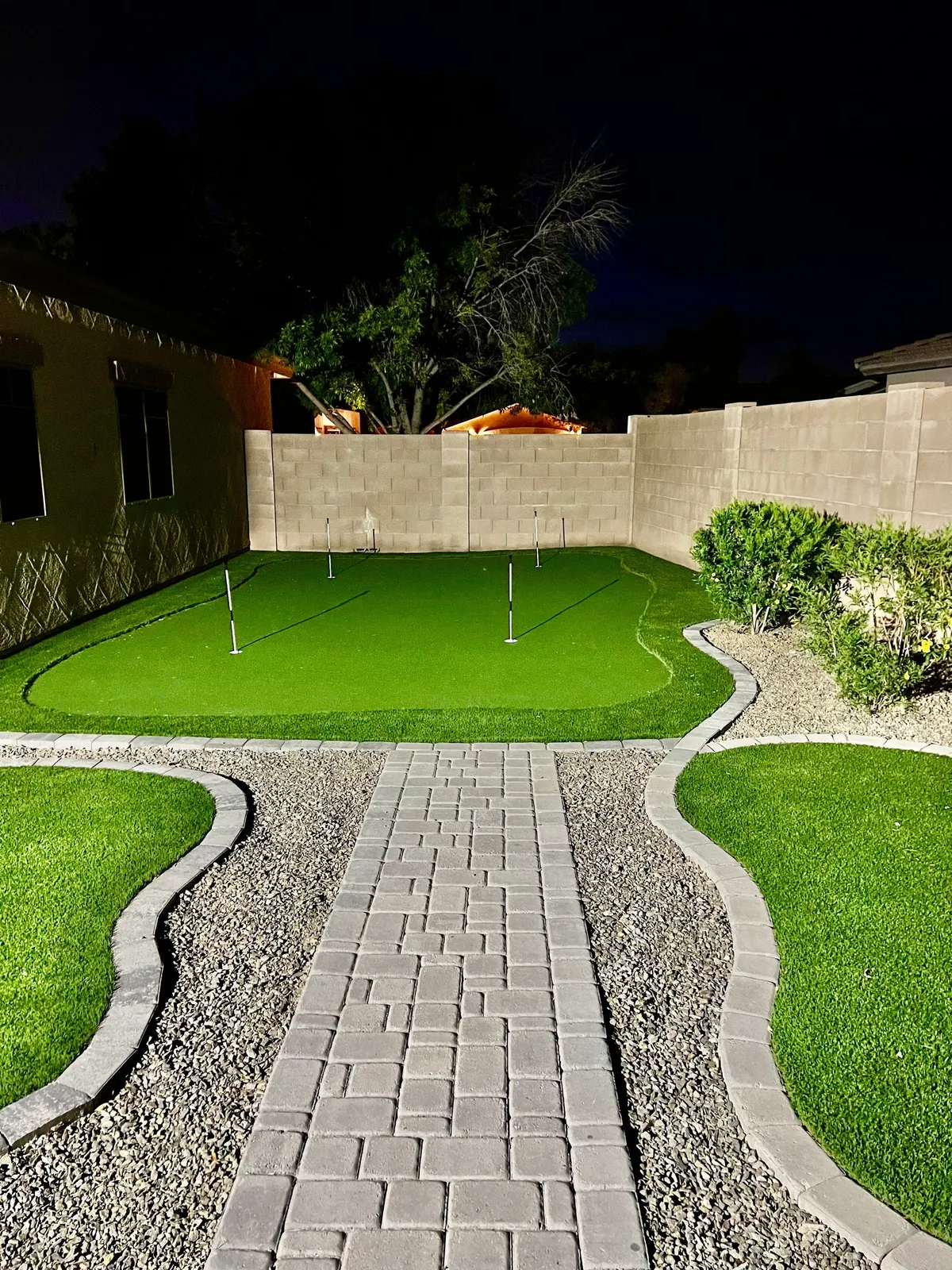 A serene outdoor putting green surrounded by greenery and landscaped pathways. The area is designed for golf practice, casual recreation, and quiet moments in nature.