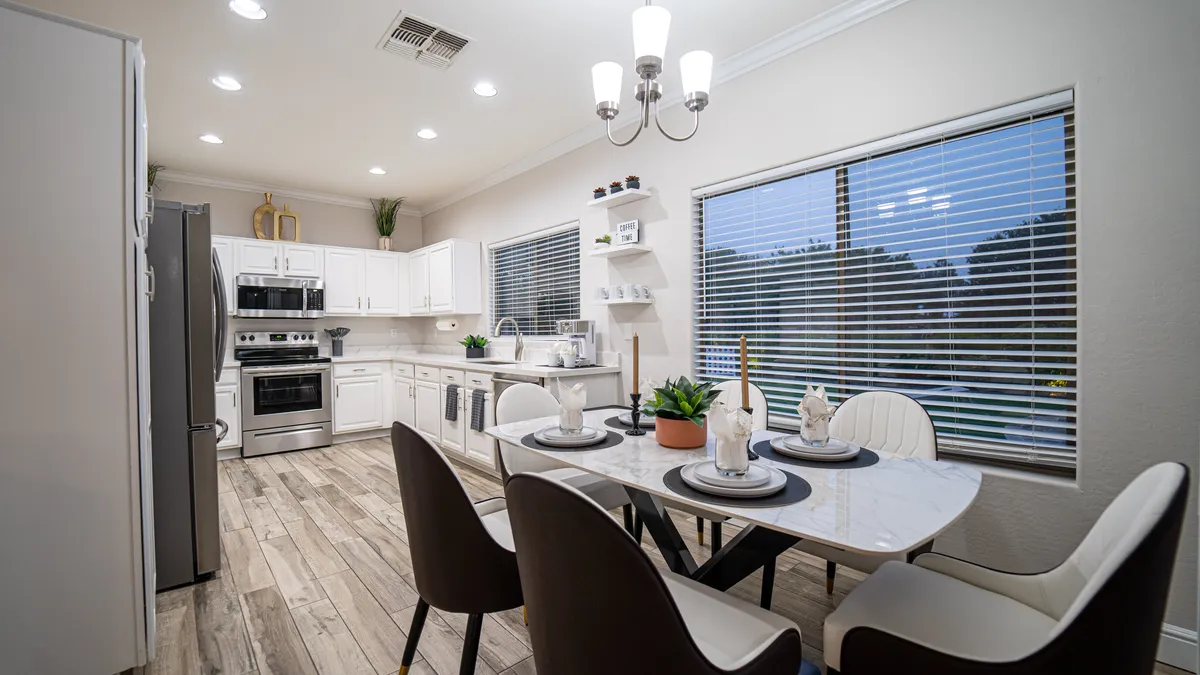 An open-concept dining area that seamlessly flows from a large dining table to a nearby kitchen island. The room is filled with natural light from large windows and adorned with a stylish chandelier, creating a warm, communal atmosphere.