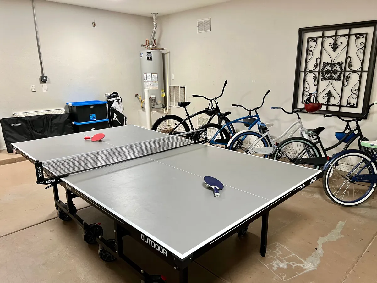 Inside, the image highlights bicycles ready for use in a recreational space with a ping pong table and storage area. The energetic mood emphasizes active lifestyles and the possibility of biking to the Queen Creek Marketplace.